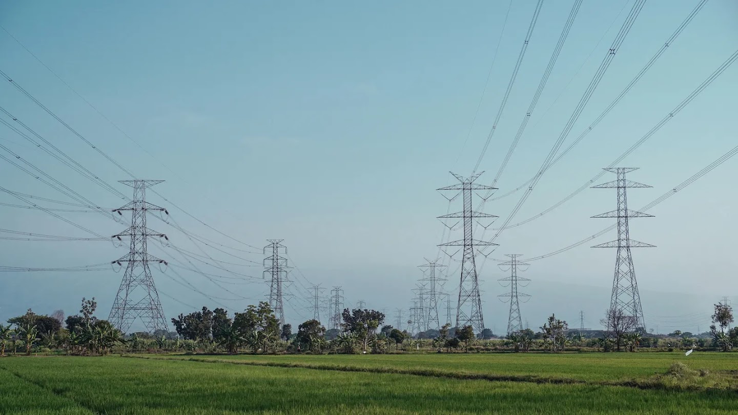Torres de alta tensión y líneas eléctricas atravesando un campo verde bajo un cielo claro.